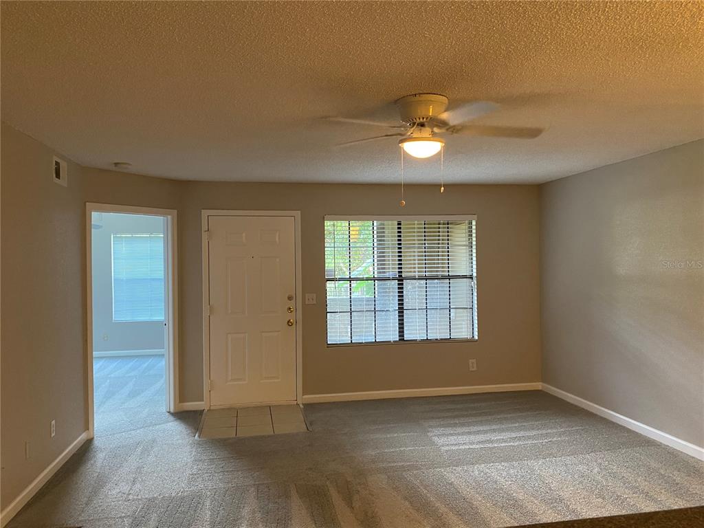 A living room with gray carpet, a ceiling fan, a white door, and a window — 400 LAKE PLACID COURT UNIT 104, ALTAMONTE SPRINGS, FL