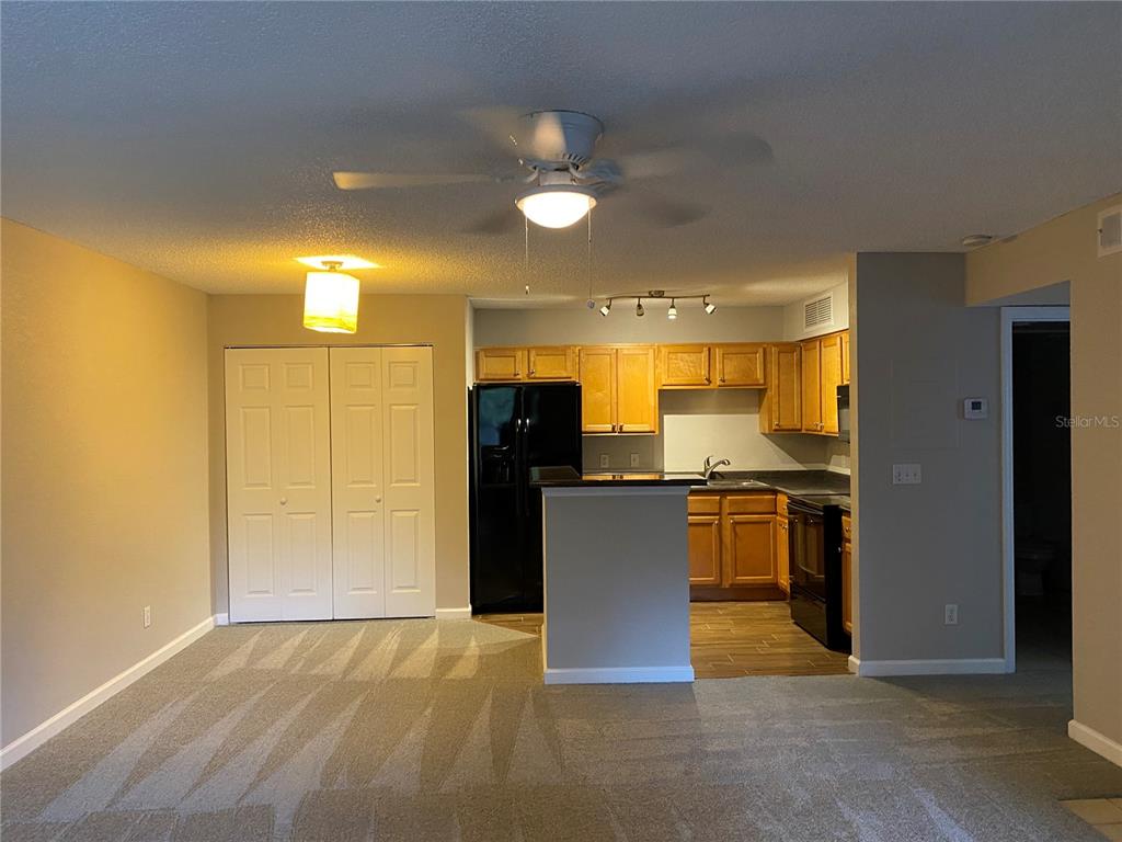 A kitchen with wood cabinets and black appliances opens to a carpeted living area — 400 LAKE PLACID COURT UNIT 104, ALTAMONTE SPRINGS, FL