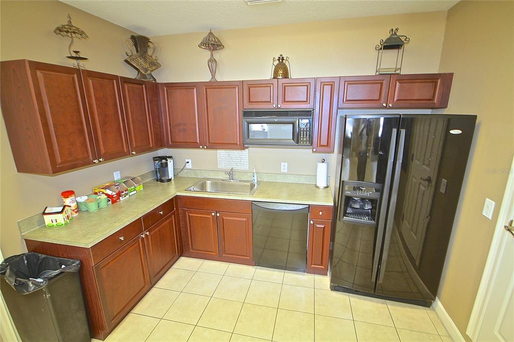 A kitchen features dark wood cabinets, a black refrigerator, a dishwasher, and light-colored countertops — 1401 TOWN PLAZA COURT UNIT 1020, WINTER SPRINGS, FL