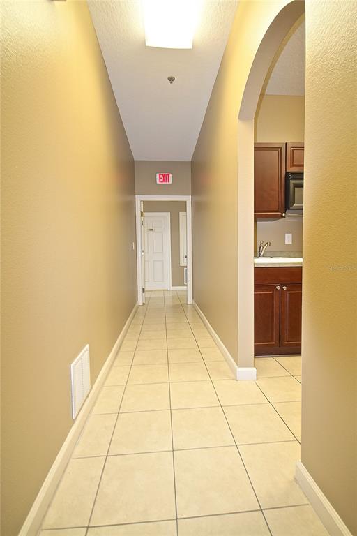 A hallway with beige tile flooring leads to an exit door, with a kitchenette visible nearby — 1401 TOWN PLAZA COURT UNIT 1020, WINTER SPRINGS, FL