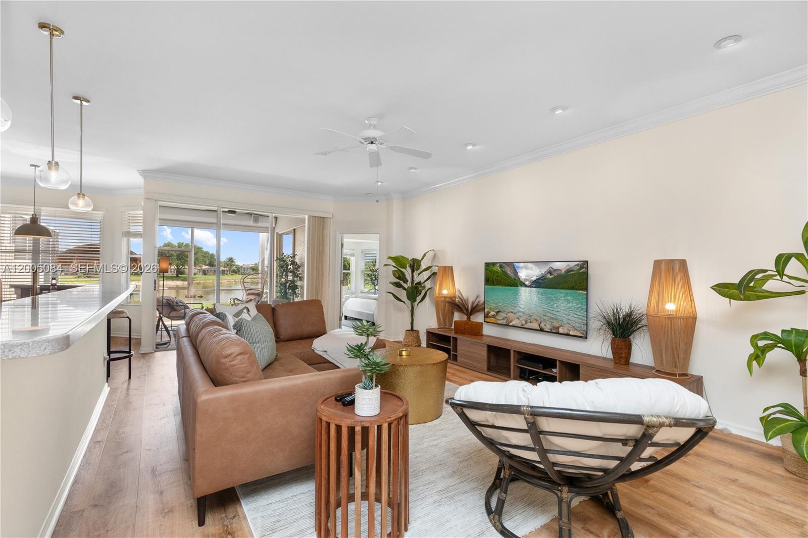 A living room features a brown leather sectional, a television, and a view of water — 1896 Crestview Way, Naples FL 34119, NAPLES, FL