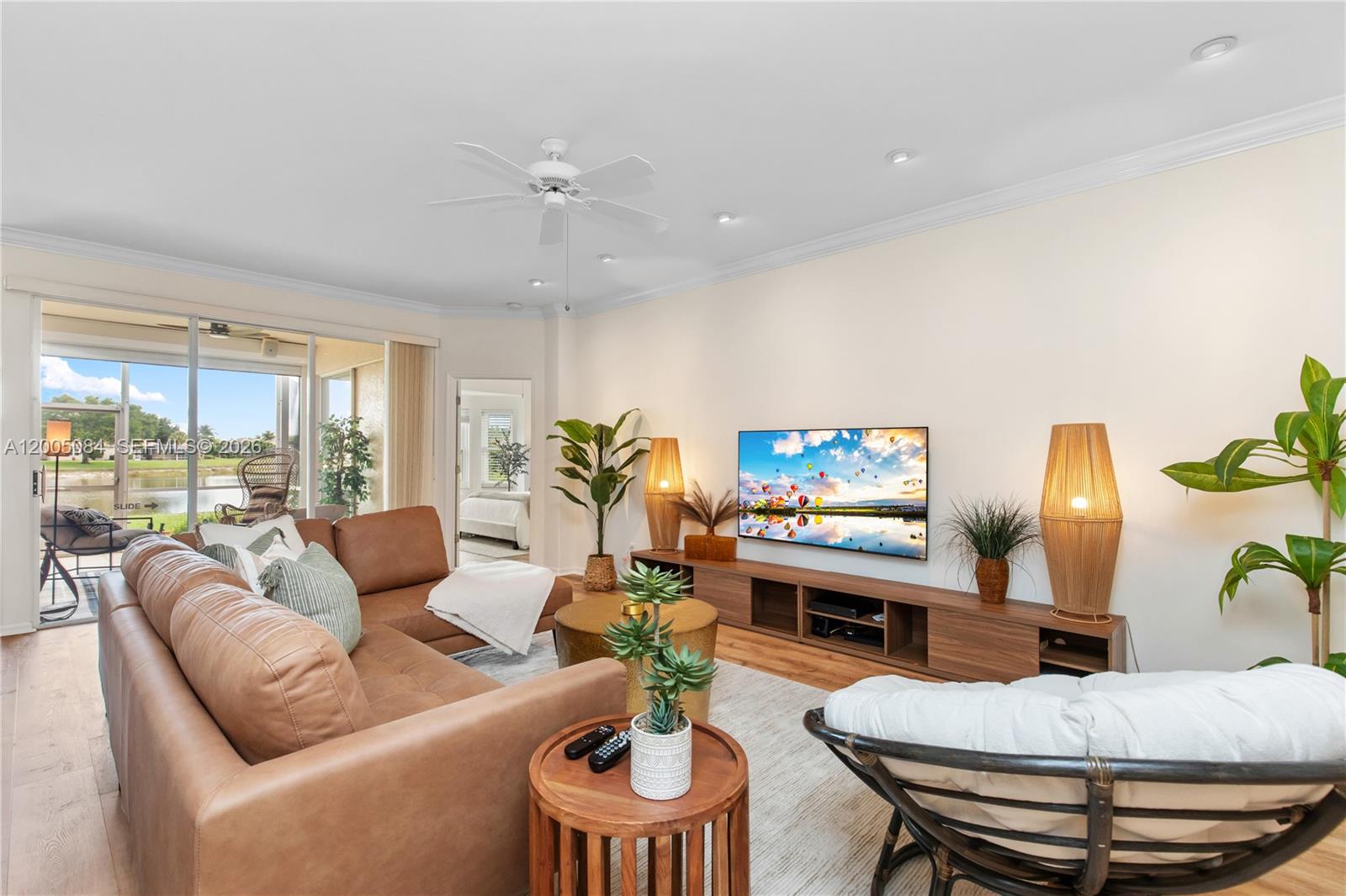 A living room features a brown leather sectional, a television, and a view of water — 1896 Crestview Way, Naples FL 34119, NAPLES, FL