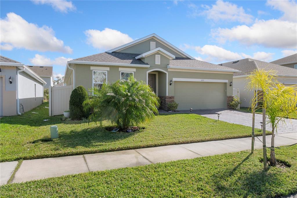 A single-story house with a tan stucco exterior, a two-car garage, and a front lawn — 1213 CRANE TALON WAY, SANFORD, FL