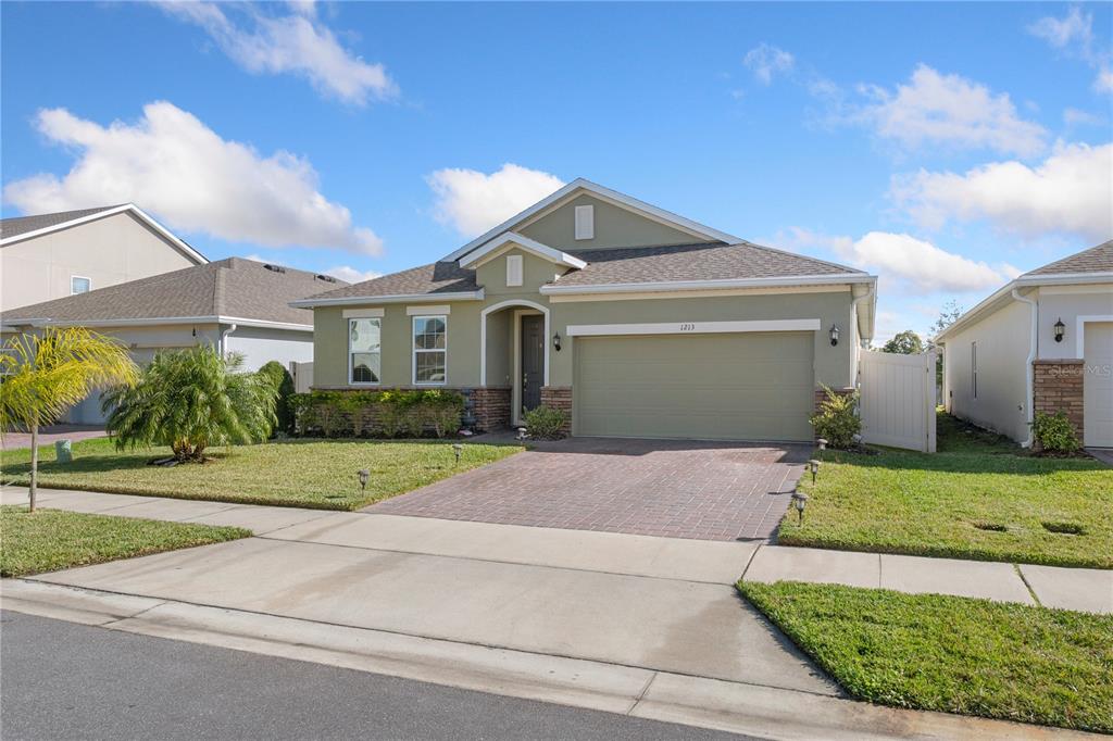 A single-story house with a green exterior, a two-car garage, and a brick driveway — 1213 CRANE TALON WAY, SANFORD, FL