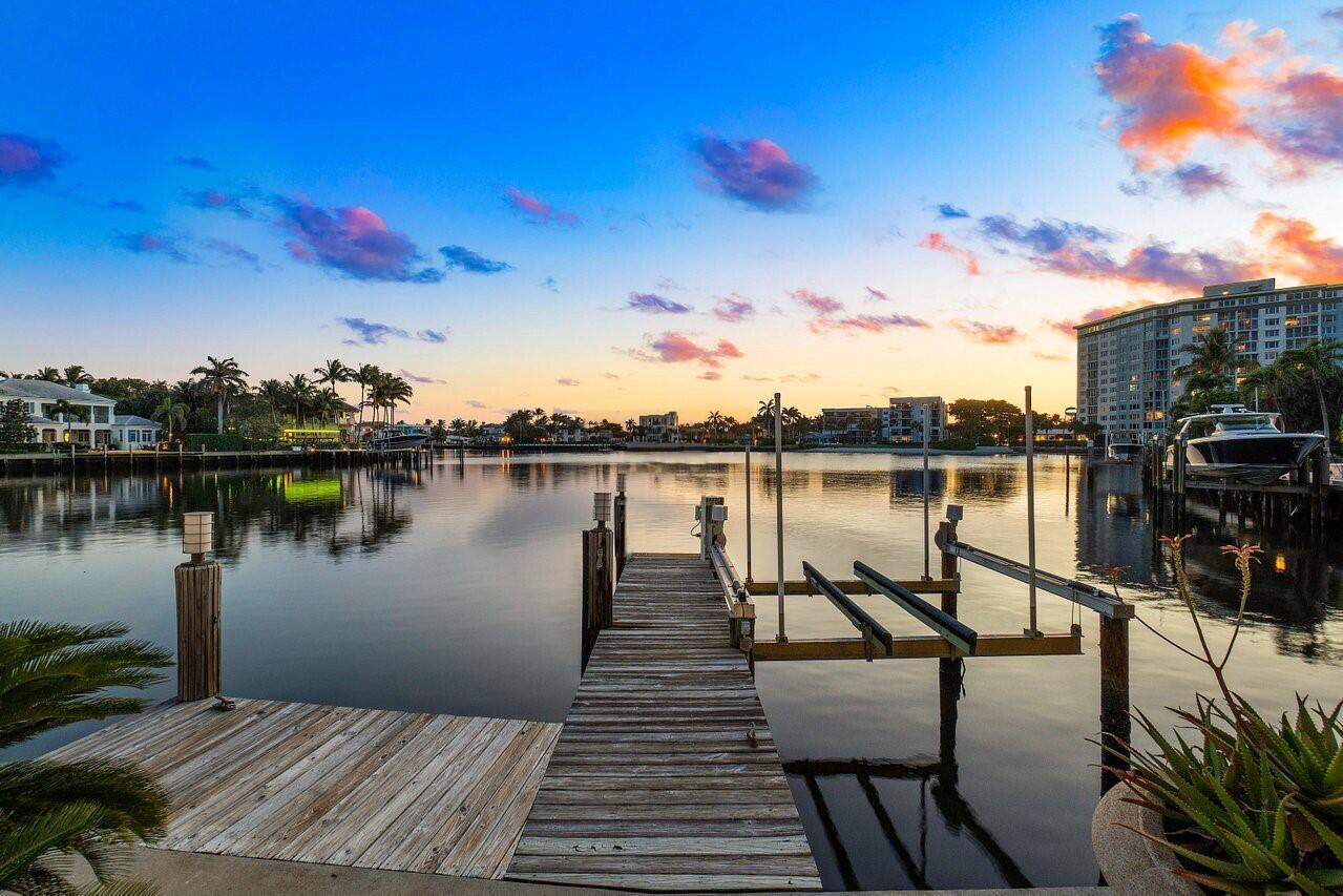 A wooden boat dock extends into a calm canal at sunset with residential buildings nearby — 616 Seasage Drive, Delray Beach FL 33483, DELRAY BEACH, FL