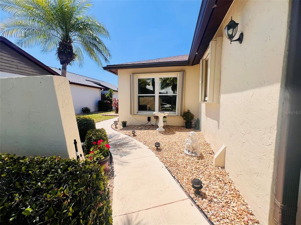 A concrete walkway leads to a house entrance with a window, gravel landscaping, and palm trees — 641 LINDEN DRIVE UNIT 328, ENGLEWOOD, FL