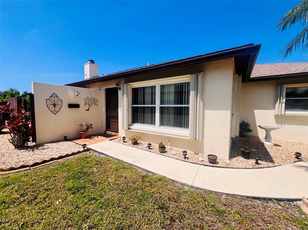 The exterior of a single-story house features a tan stucco facade, a walkway, and landscaping — 641 LINDEN DRIVE UNIT 328, ENGLEWOOD, FL