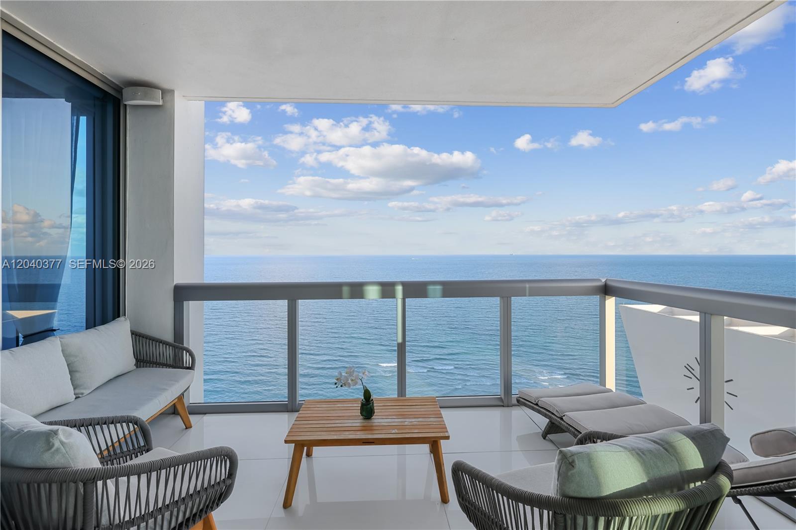 A balcony with outdoor furniture overlooks the ocean under a blue sky with clouds — 6899 Collins Ave # 2208, Miami Beach FL 33141, MIAMI BEACH, FL