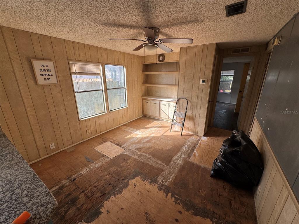 A room with wood-paneled walls, a ceiling fan, built-in shelving, and exposed subflooring — 10559 BAY HILLS CIRCLE, THONOTOSASSA, FL