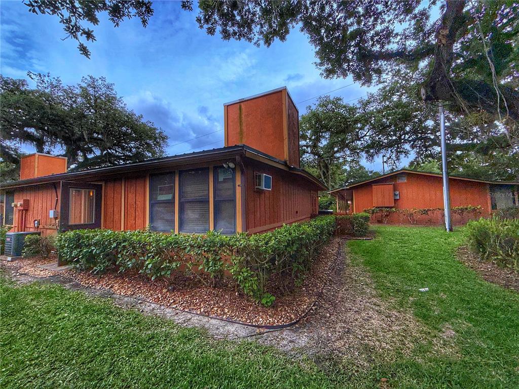 An exterior view of a single-story house with wood siding and a prominent chimney — 403 COTTAGE CIRCLE E UNIT 403, LAKE WALES, FL