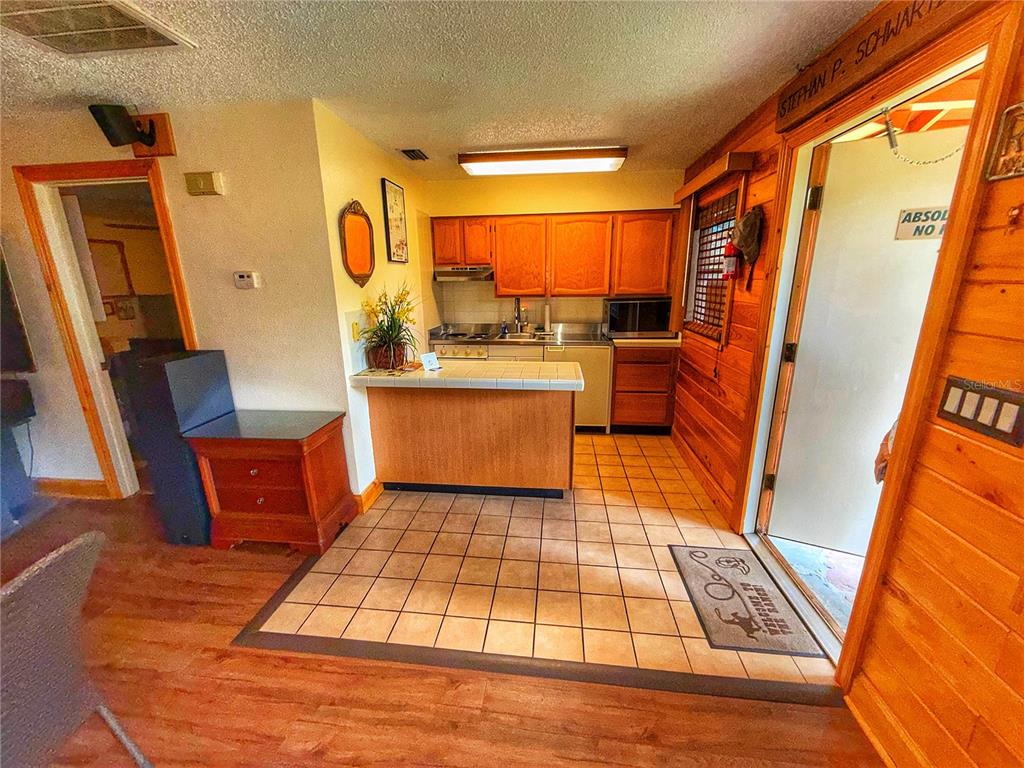 A kitchen with wood cabinets, tiled counters, and a tiled floor opens to a room — 403 COTTAGE CIRCLE E UNIT 403, LAKE WALES, FL