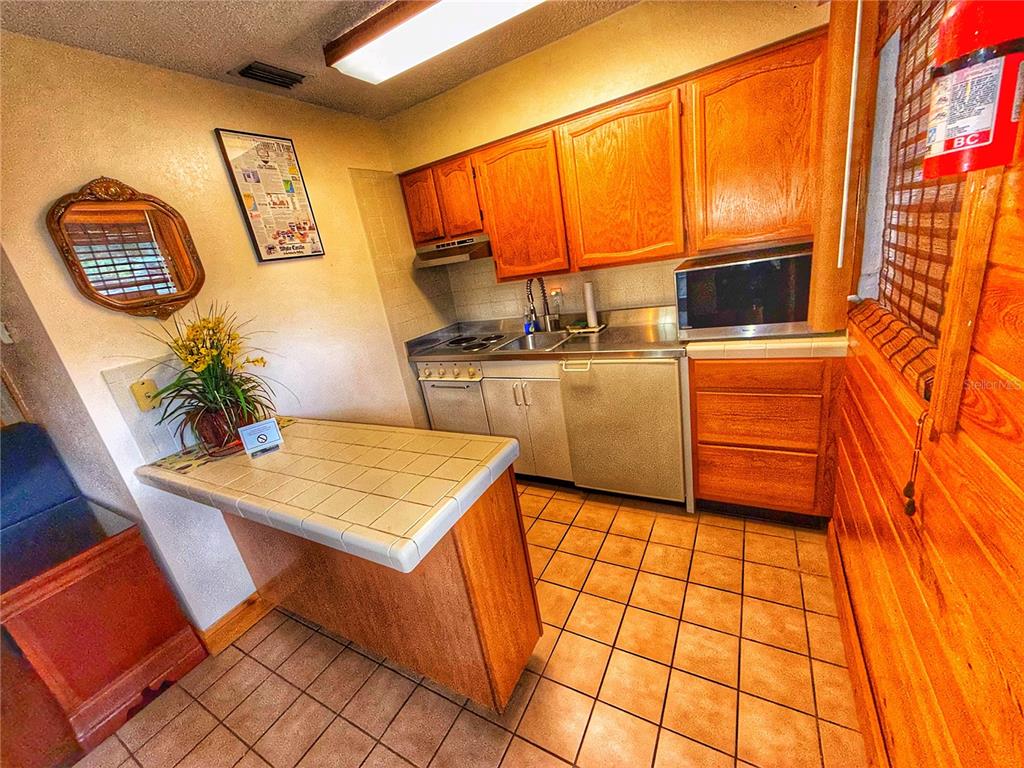 A kitchen features wood cabinets, tile countertops, a tiled floor, and a small breakfast bar — 403 COTTAGE CIRCLE E UNIT 403, LAKE WALES, FL