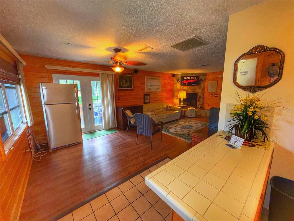 A living room with wood-paneled walls, a fireplace, and a tiled kitchen counter in front — 403 COTTAGE CIRCLE E UNIT 403, LAKE WALES, FL
