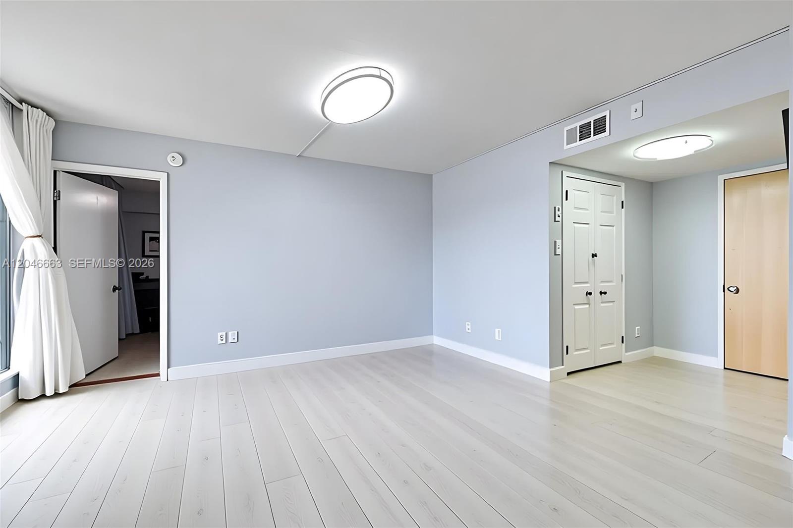 An empty room features light-colored wood flooring, pale blue walls, and two ceiling light fixtures — 2075 SW 122nd Ave # 505, Miami FL 33175, MIAMI, FL