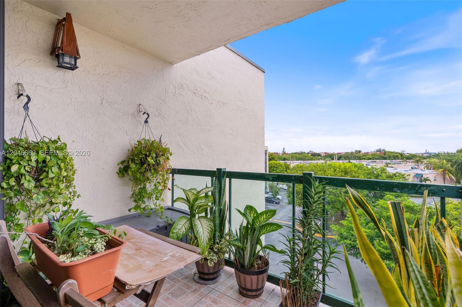 A balcony features potted plants, a small table, and a view of trees and buildings — 2075 SW 122nd Ave # 505, Miami FL 33175, MIAMI, FL