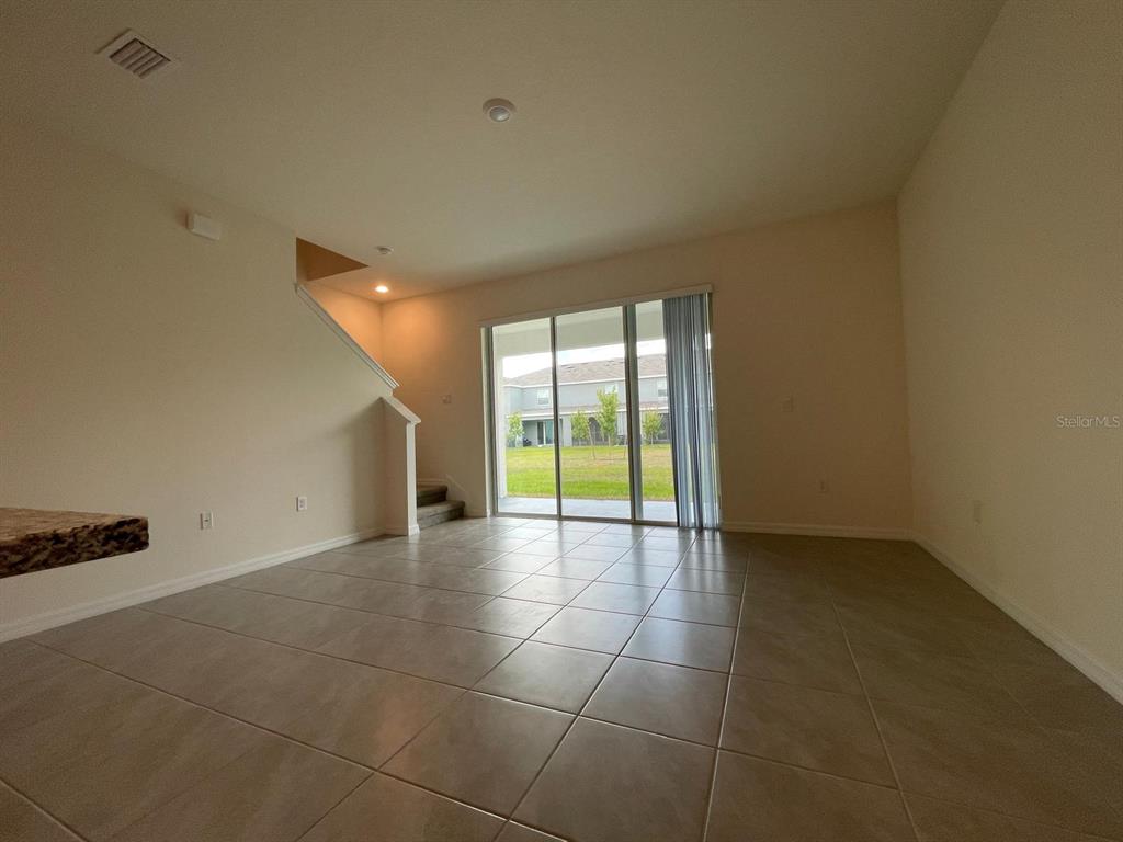 An open living area features tile flooring, a staircase, and sliding glass doors to outside — 32930 REGENT CANAL STREET, WESLEY CHAPEL, FL