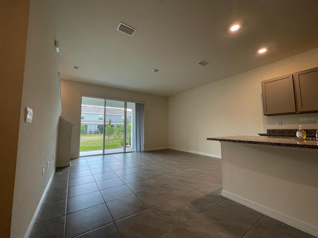 An open-concept living area features tile flooring, a kitchen island, and sliding glass patio doors — 32930 REGENT CANAL STREET, WESLEY CHAPEL, FL