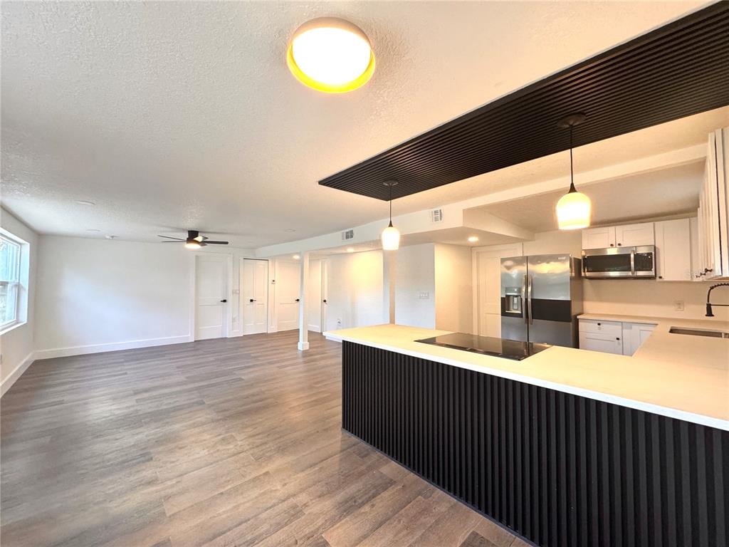 A kitchen with white cabinets and a stainless steel stove overlooks an open living area — 1135 CHEROKEE DRIVE, KISSIMMEE, FL