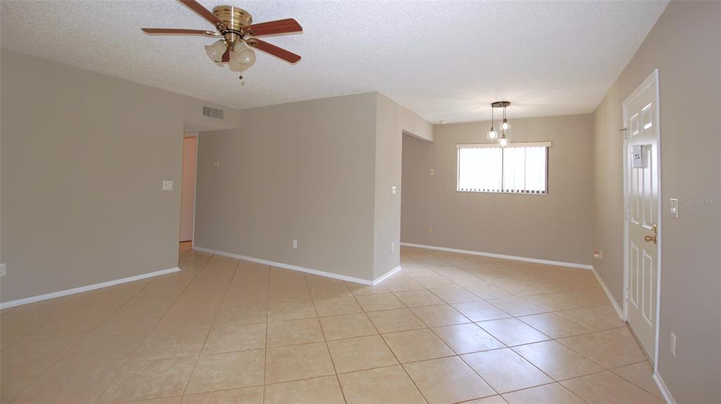 An open-concept living area features beige walls, light-colored tile flooring, and a ceiling fan — 3300 FOX CHASE CIRCLE N UNIT 216, PALM HARBOR, FL