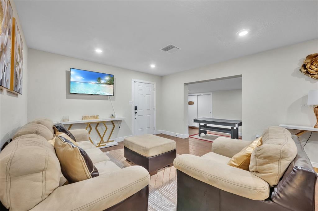 A living room features a beige sofa, a matching ottoman, and a wall-mounted television — 1221 ELINORE DRIVE, ORLANDO, FL
