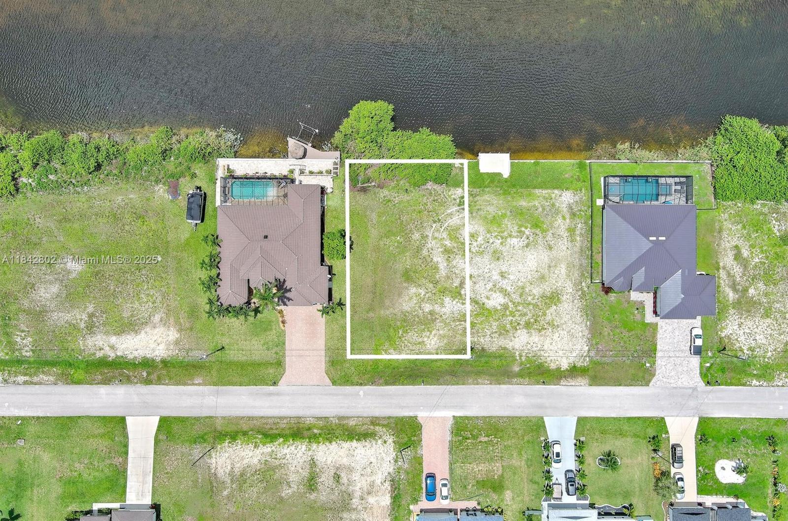 This aerial view shows a vacant residential lot situated between two houses along a canal — 401 NW 24th Ter, Cape Coral FL 33993, CAPE CORAL, FL