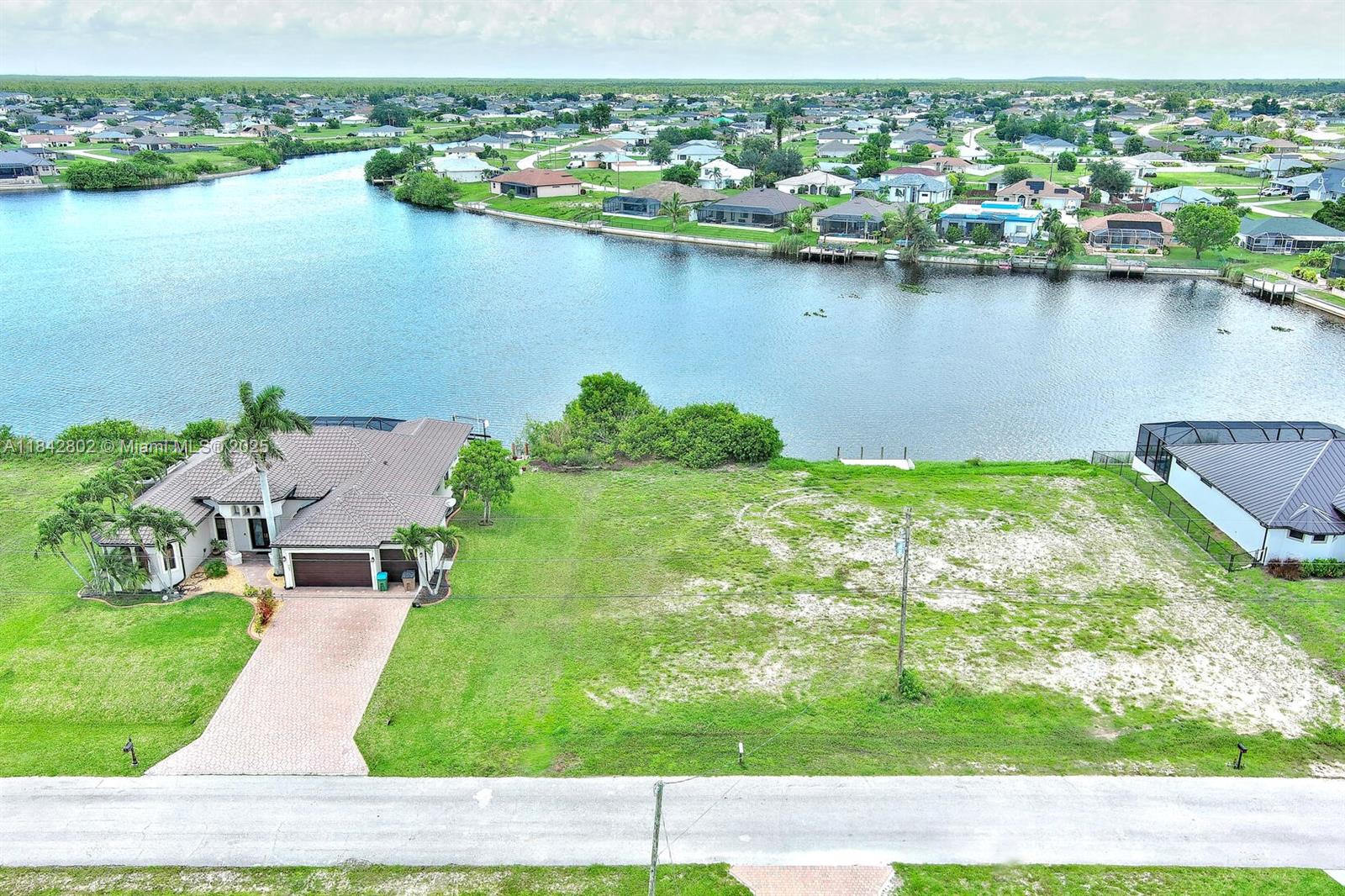 An aerial view shows a house next to a large vacant lot bordering a lake — 401 NW 24th Ter, Cape Coral FL 33993, CAPE CORAL, FL