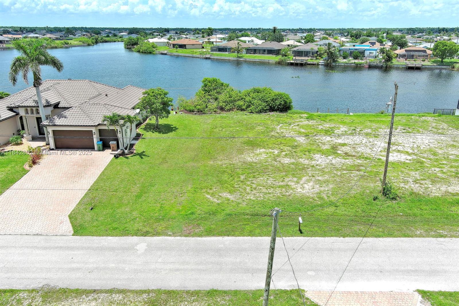An aerial view shows a vacant grassy lot next to a house by a canal — 401 NW 24th Ter, Cape Coral FL 33993, CAPE CORAL, FL