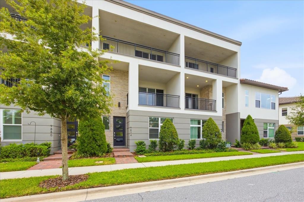 A three-story modern apartment building with balconies, stone accents, and a landscaped front lawn — 9874 BUCKLOW HILL DRIVE, ORLANDO, FL