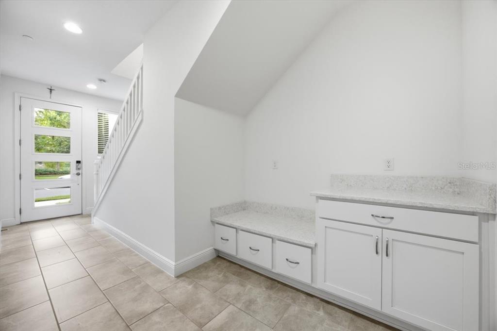 A white entryway features a built-in bench with drawers, cabinetry, and light-colored tile flooring — 9874 BUCKLOW HILL DRIVE, ORLANDO, FL
