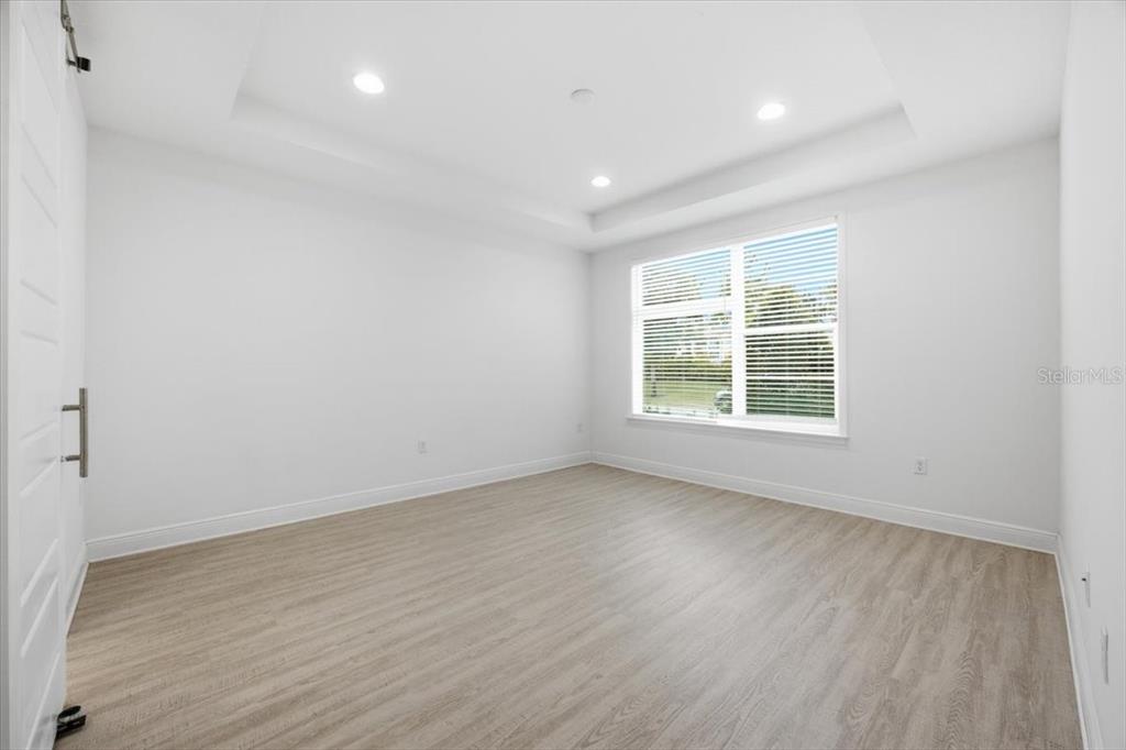 An empty bedroom features white walls, light wood-look flooring, and a tray ceiling with recessed lighting — 9874 BUCKLOW HILL DRIVE, ORLANDO, FL