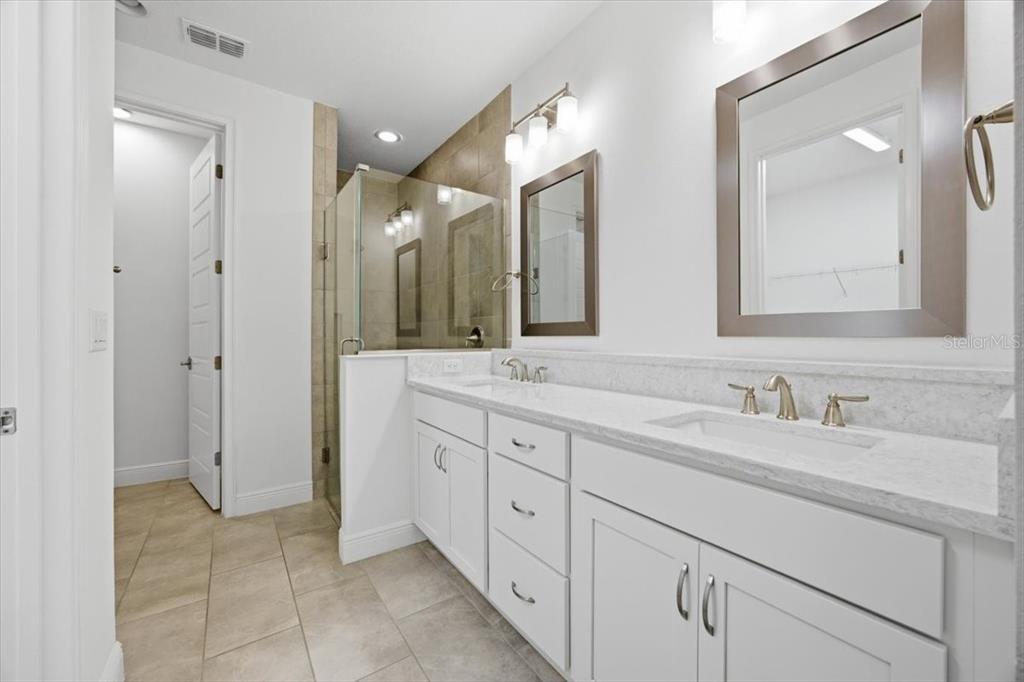 A bathroom features a double vanity with white cabinets, stone countertops, and a glass-enclosed shower — 9874 BUCKLOW HILL DRIVE, ORLANDO, FL