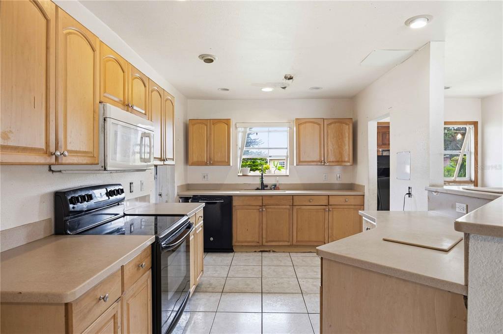 A kitchen features light wood cabinets, laminate countertops, a black stove, and tiled flooring — 21378 PERCY AVENUE, PORT CHARLOTTE, FL