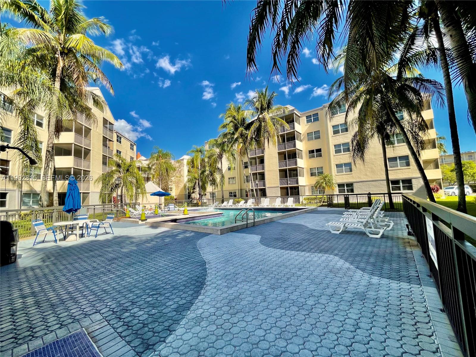 A swimming pool area with lounge chairs and palm trees surrounded by multi-story apartment buildings — 8255 Lake Dr # 102, Doral FL 33166, DORAL, FL