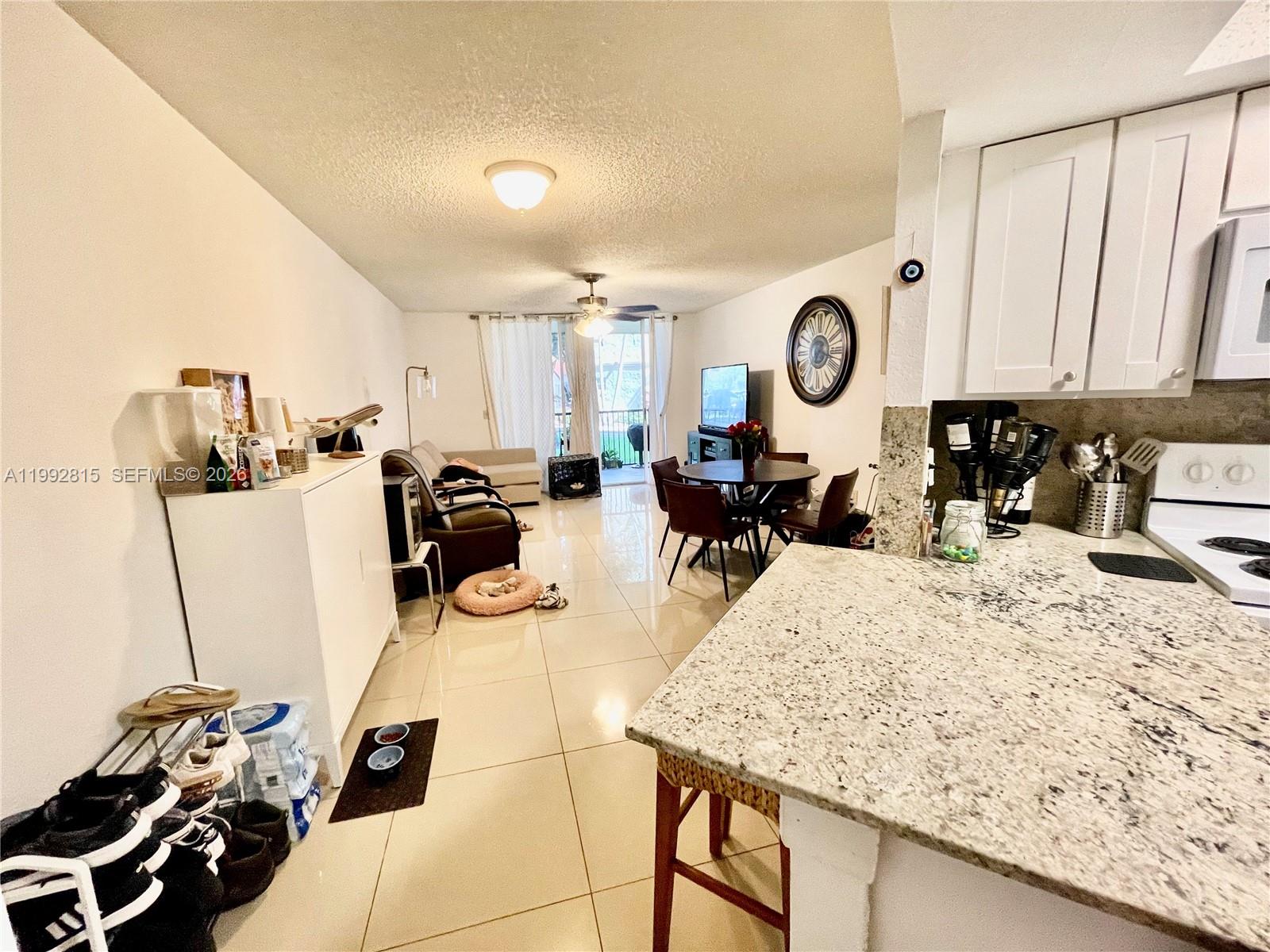 This open-concept living and dining area features tile flooring and a granite-topped kitchen island — 8255 Lake Dr # 102, Doral FL 33166, DORAL, FL