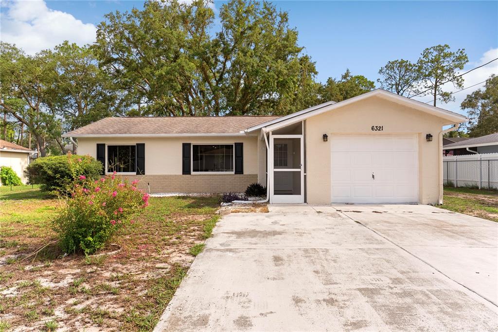 A single-story house with a beige exterior, a white garage door, and a concrete driveway — 6321 PIEDMONT DRIVE, SPRING HILL, FL