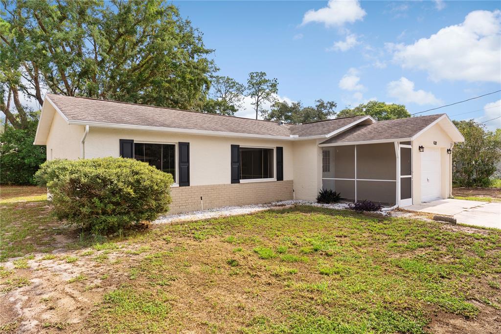 A single-story house with a tan exterior, brick accents, and a screened-in front porch — 6321 PIEDMONT DRIVE, SPRING HILL, FL