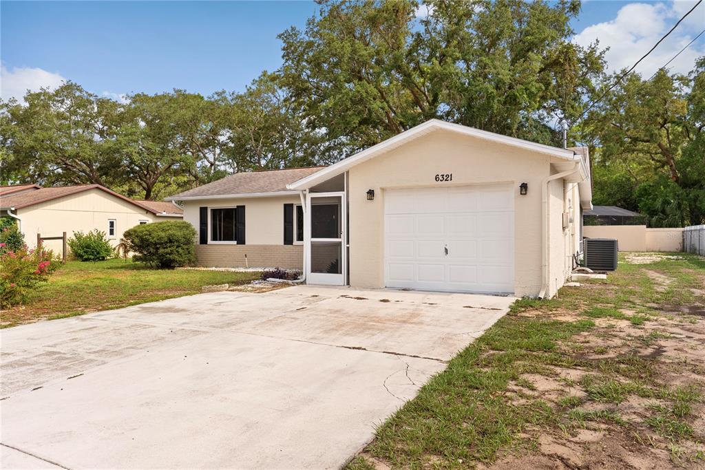 A single-story house with a white garage, a concrete driveway, and a screened front porch — 6321 PIEDMONT DRIVE, SPRING HILL, FL