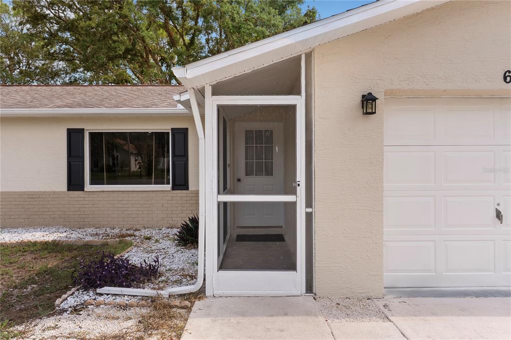 The exterior of a house features a screened front entryway, a garage, and a window — 6321 PIEDMONT DRIVE, SPRING HILL, FL