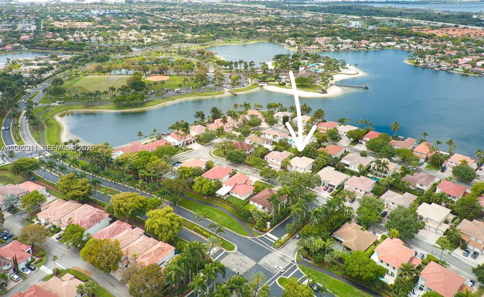 An aerial view shows a residential neighborhood with houses, palm trees, and a large lake — 6772 NW 111th Ave, Doral FL 33178, DORAL, FL