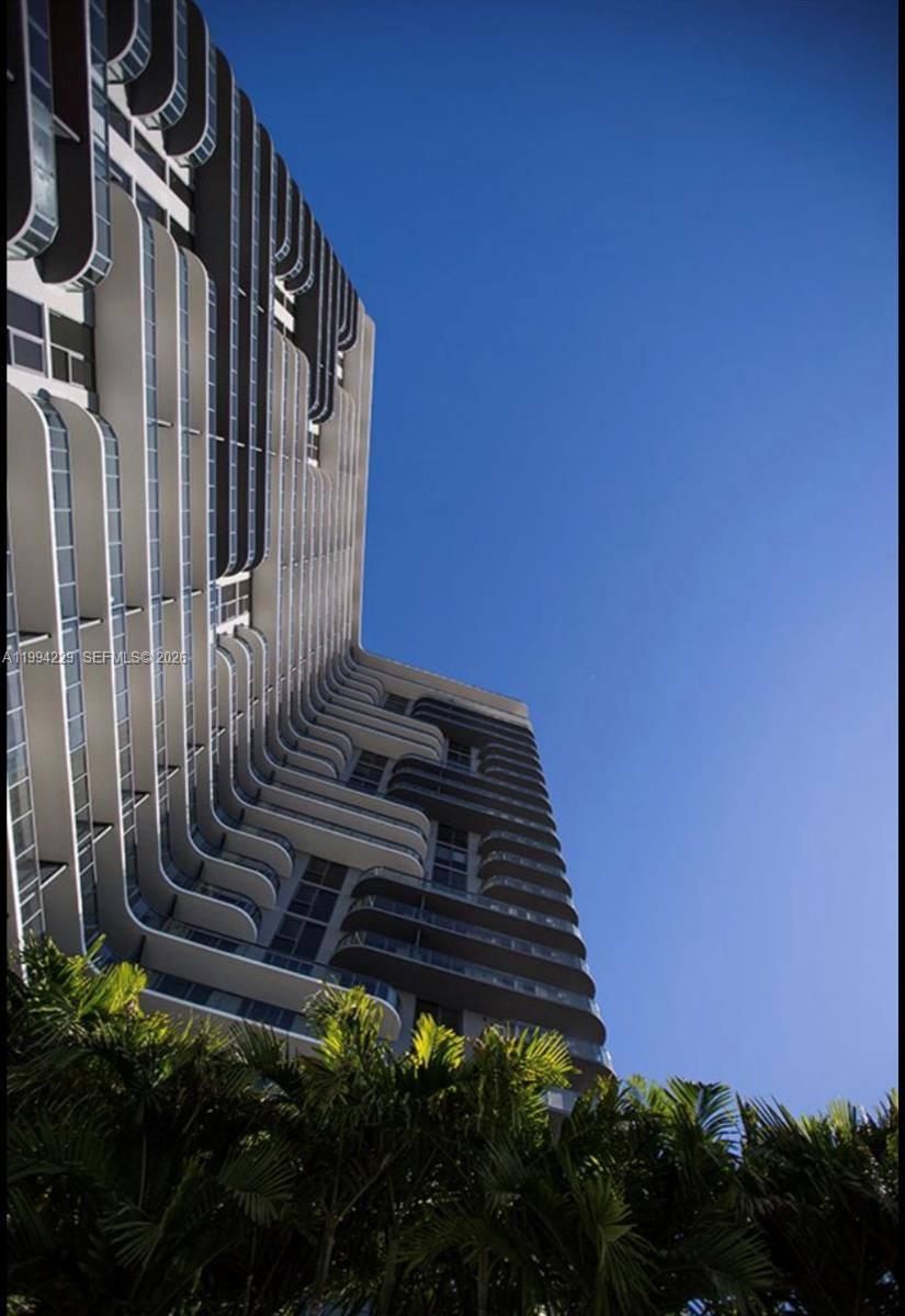 A low-angle view of a modern high-rise building with curved balconies against a blue sky — 121 NE 34th St # 2311, Miami FL 33137, MIAMI, FL