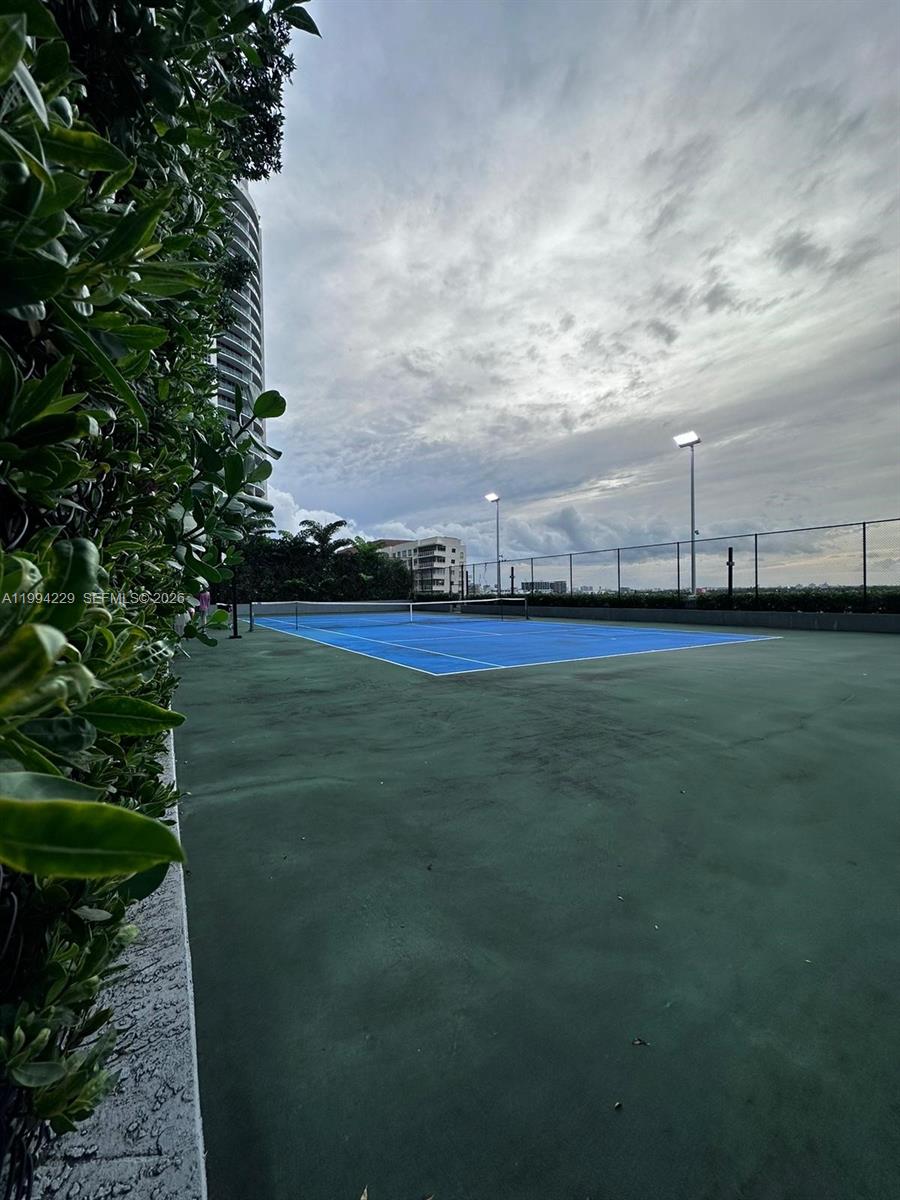 An outdoor blue tennis court is surrounded by a fence and a tall building — 121 NE 34th St # 2311, Miami FL 33137, MIAMI, FL