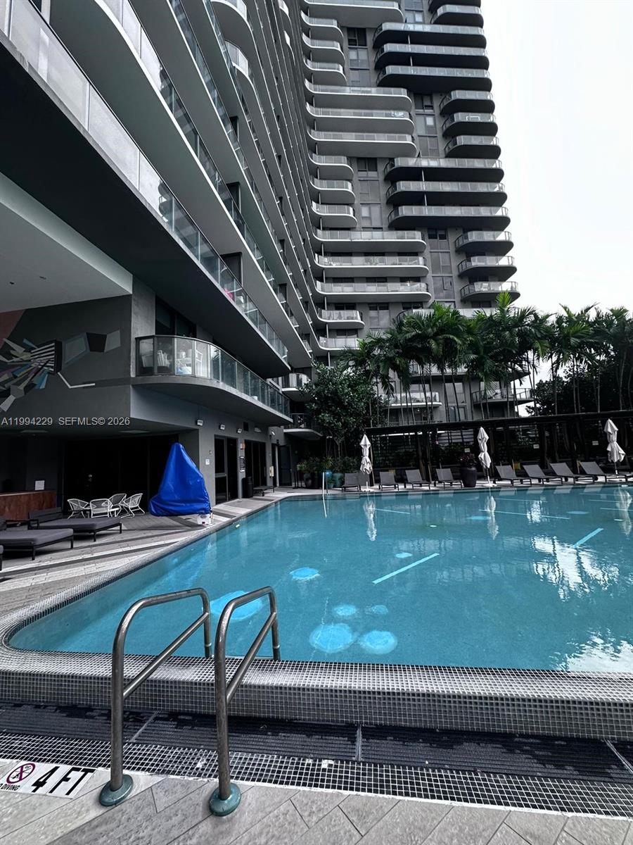A swimming pool sits beside a modern high-rise building with tiered balconies and palm trees — 121 NE 34th St # 2311, Miami FL 33137, MIAMI, FL