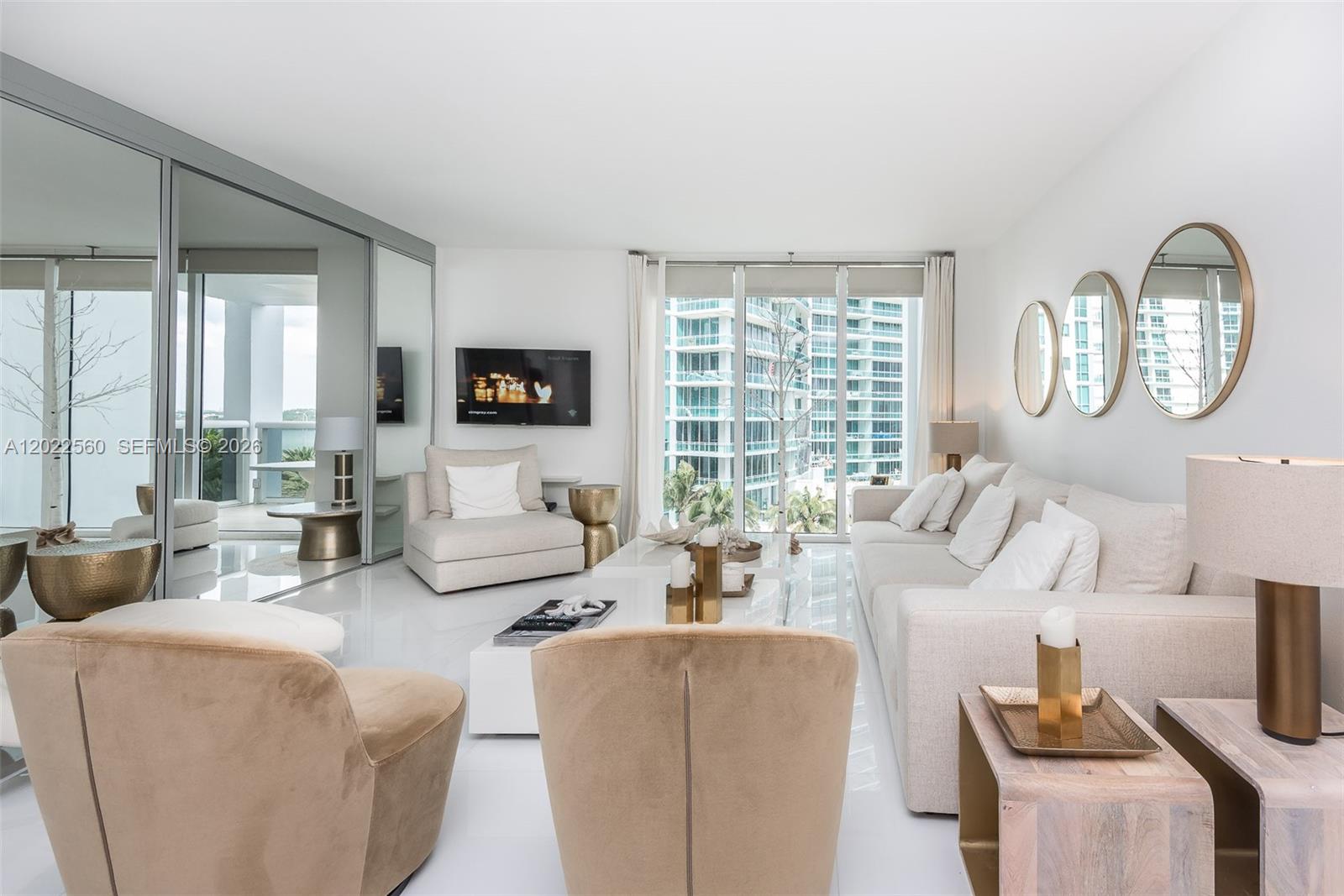 A modern living room features white tile floors, neutral furniture, and a large mirrored wall — 10275 Collins Ave # 706, Bal Harbour FL 33154, BAL HARBOUR, FL