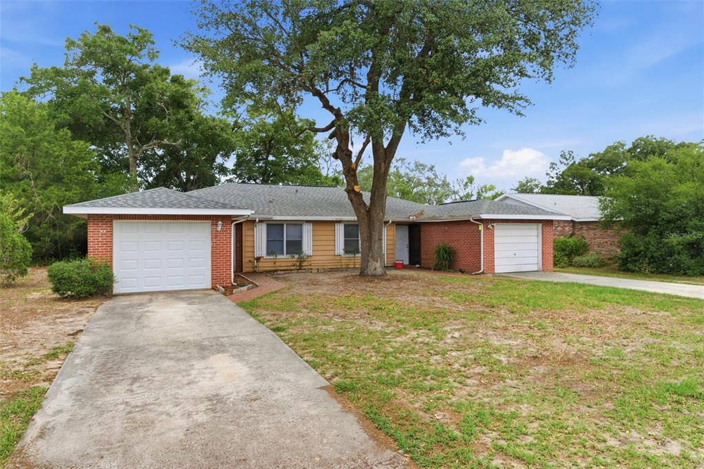 A single-story brick and wood-sided house features two garage doors and a large front tree — 8124 OMAHA CIRCLE, SPRING HILL, FL