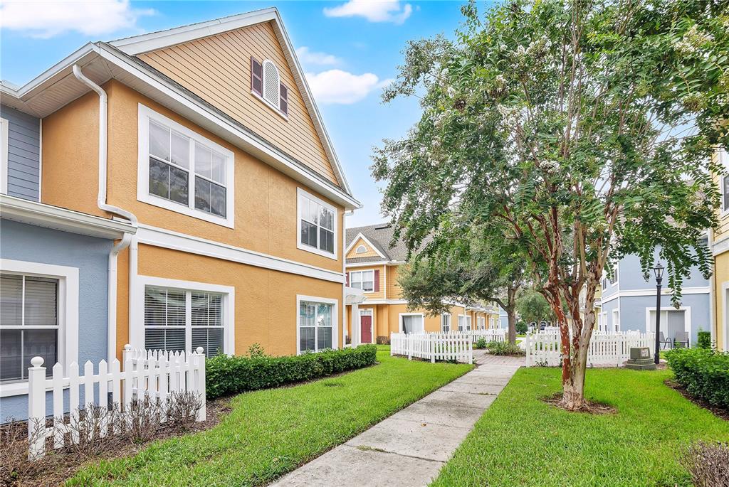 A two-story apartment building with yellow and blue siding, a white picket fence, and landscaping — 4005 SAN SEBASTIAN DRIVE UNIT 101, KISSIMMEE, FL