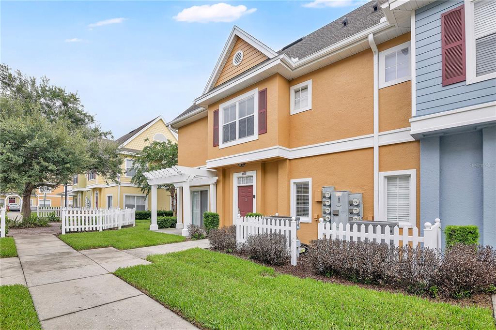 A two-story yellow townhouse with a white pergola, picket fence, and a red front door — 4005 SAN SEBASTIAN DRIVE UNIT 101, KISSIMMEE, FL