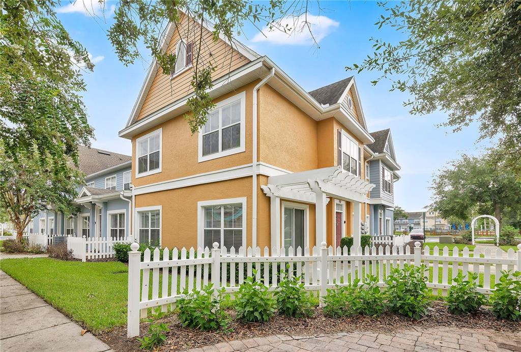A two-story yellow townhouse with a white picket fence and a pergola over the entrance — 4005 SAN SEBASTIAN DRIVE UNIT 101, KISSIMMEE, FL