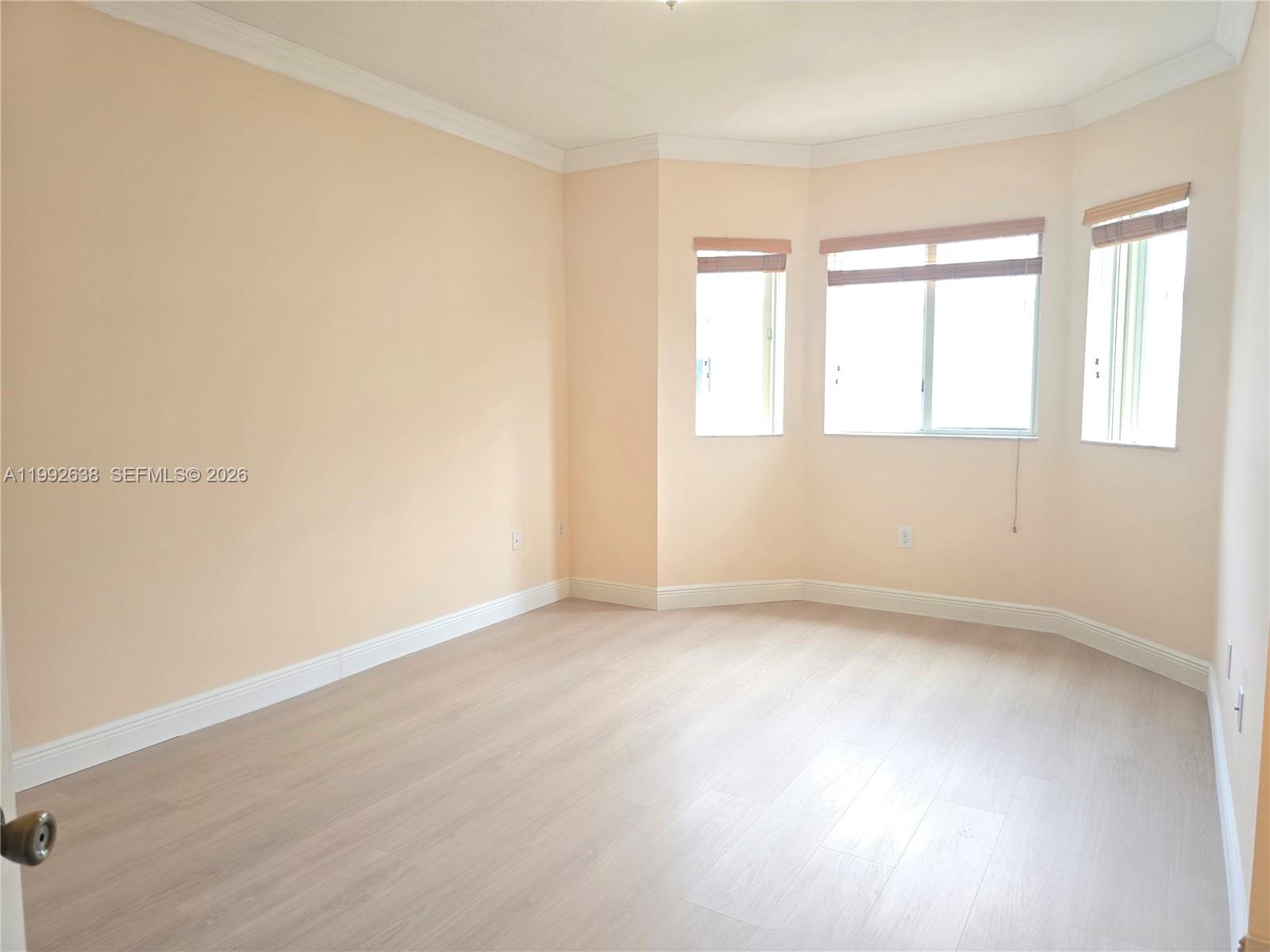 An empty room features light-colored wood-look flooring, peach walls, and a bay window — 8421 SW 124th Ave # 101, Miami FL 33183, MIAMI, FL