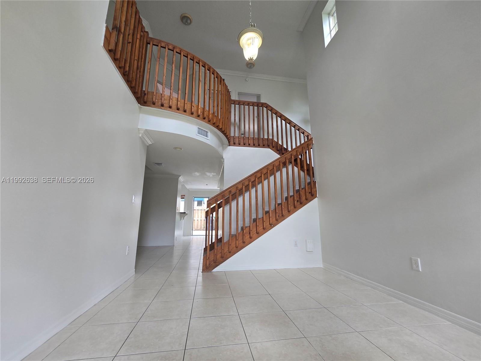 An entryway features a curved wooden staircase, tile flooring, and a high ceiling with pendant lighting — 8421 SW 124th Ave # 101, Miami FL 33183, MIAMI, FL