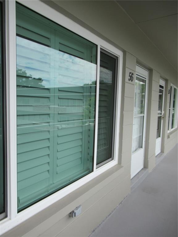 A view of a building exterior featuring a large window with shutters and a door — 2426 PERSIAN DRIVE UNIT 56, CLEARWATER, FL